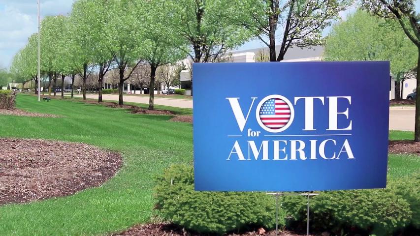 Corrugated plastic yard sign staked in a lawn along a tree-lined street