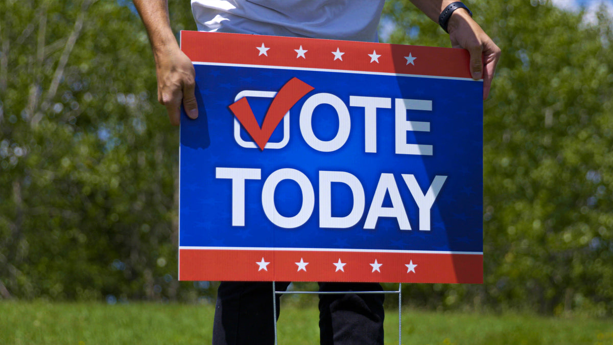 Corrugated plastic yard sign held at close range on its wire step stake, showing the fluted panel