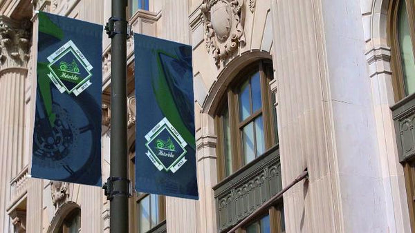 Pair of vinyl pole banners mounted on brackets to a street light outside a stone building