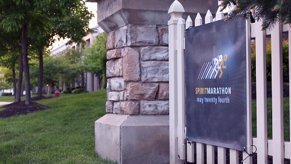 Mesh banner zip-tied to a picket fence, with the perforated weave letting light through