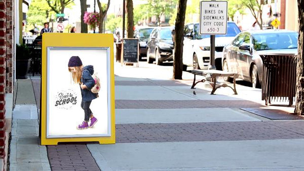 PVC sign panel mounted in a yellow A-frame sidewalk sign holder outside a storefront