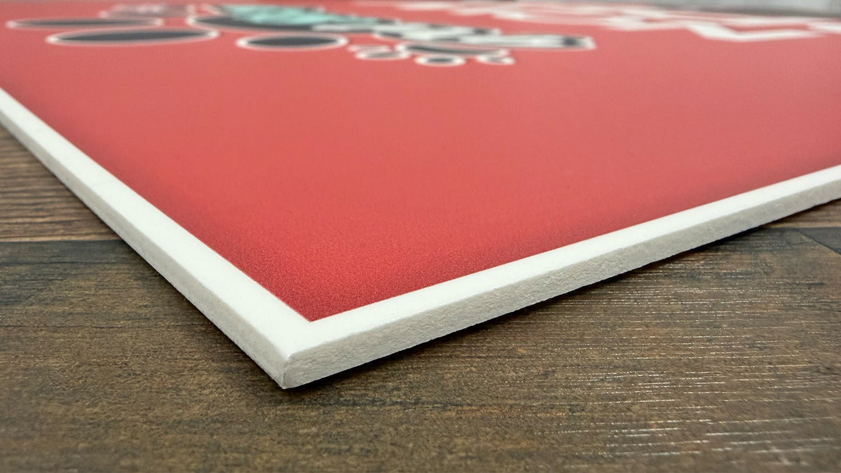 Close-up of a PVC sign corner on a table, showing the smooth white board edge and matte printed face