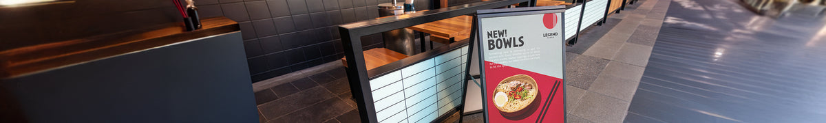 Wide view of a PVC promotional sign in an A-frame holder beside restaurant seating